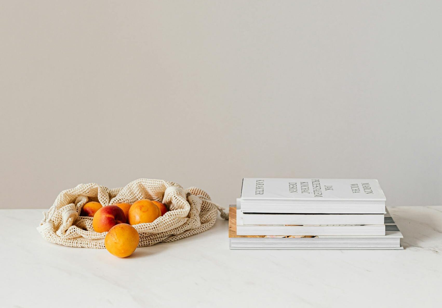 Composition of canvas bag with fresh ripe apricots placed on white table near stack of various books