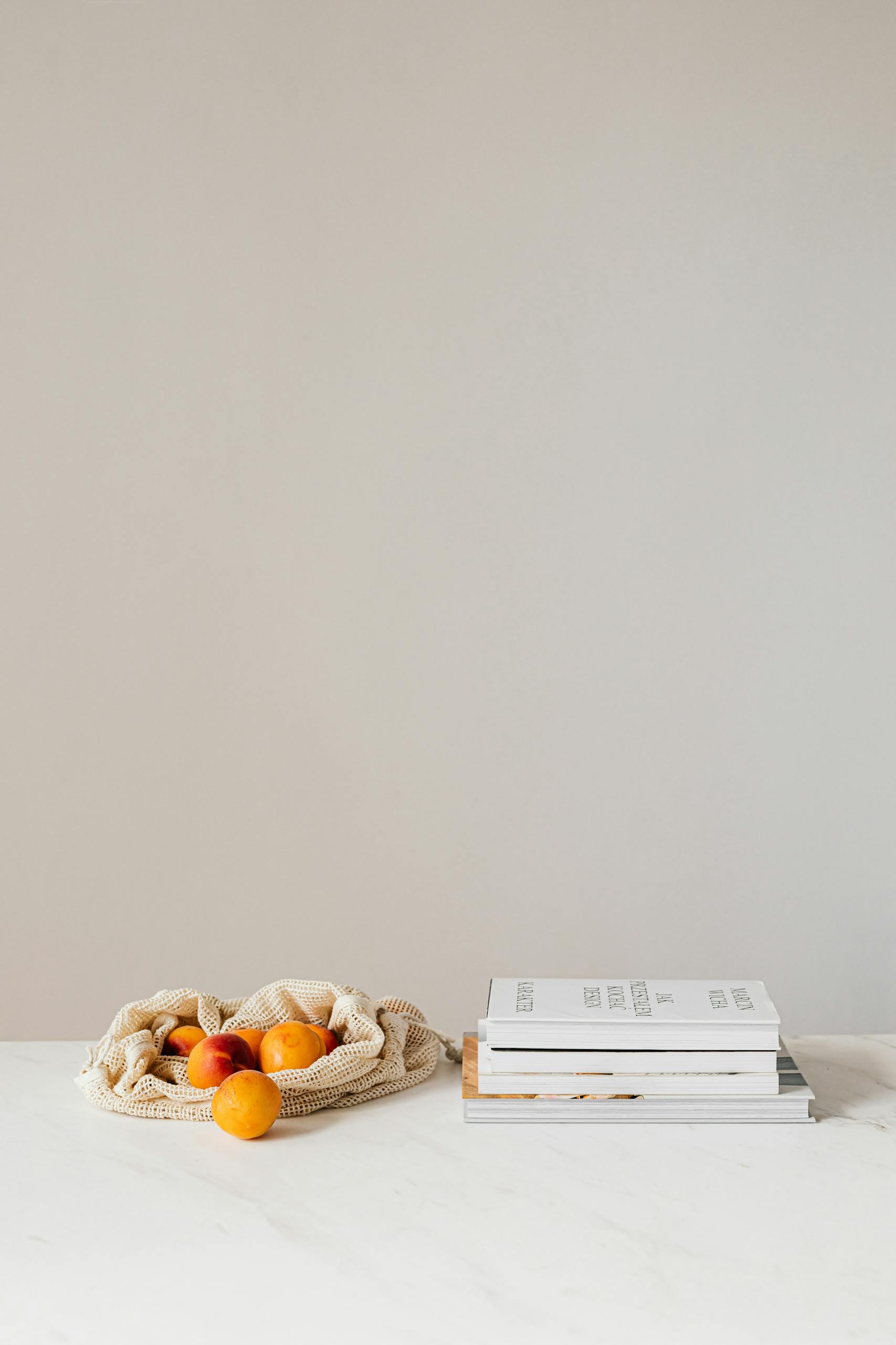 Composition of canvas bag with fresh ripe apricots placed on white table near stack of various books