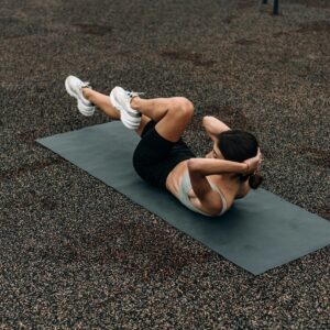 A woman performing an abdominal exercise outdoors on a mat, viewed from above.
