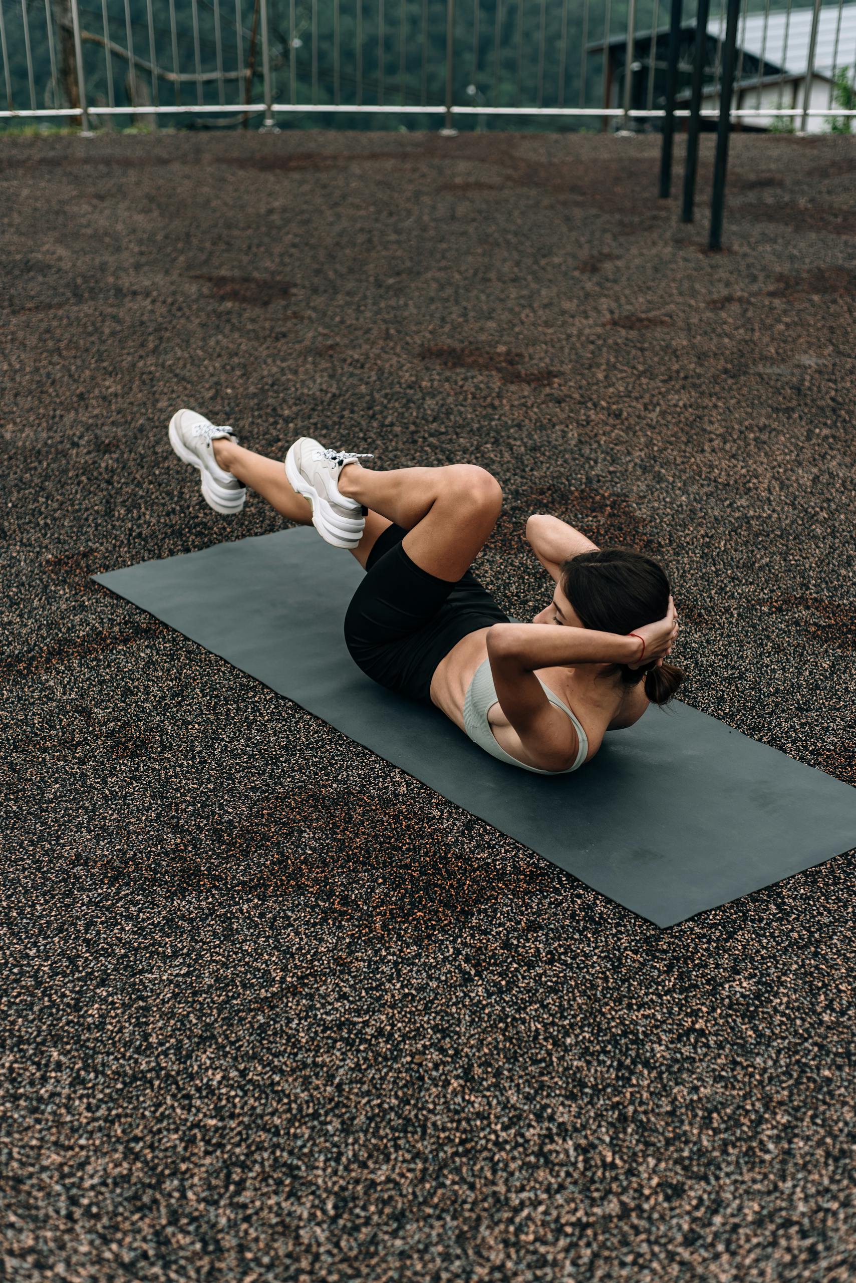A woman performing an abdominal exercise outdoors on a mat, viewed from above.